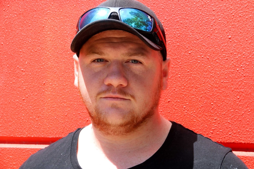 Close head shot of a man wearing a cap against a red wall