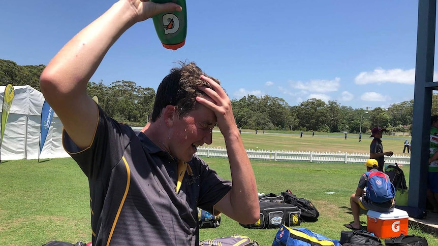 A teenage cricketer squeezes water over his head to cool down
