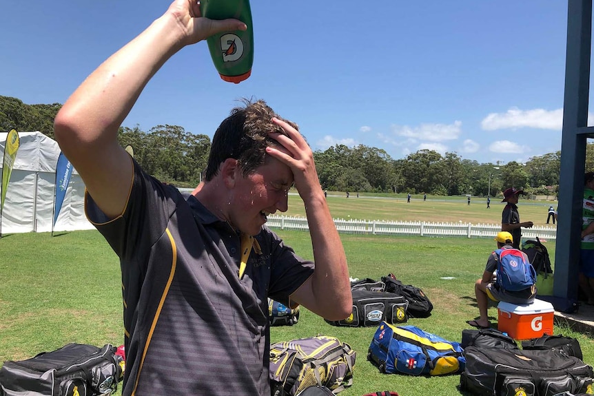A teenage cricketer squeezes water over his head to cool down
