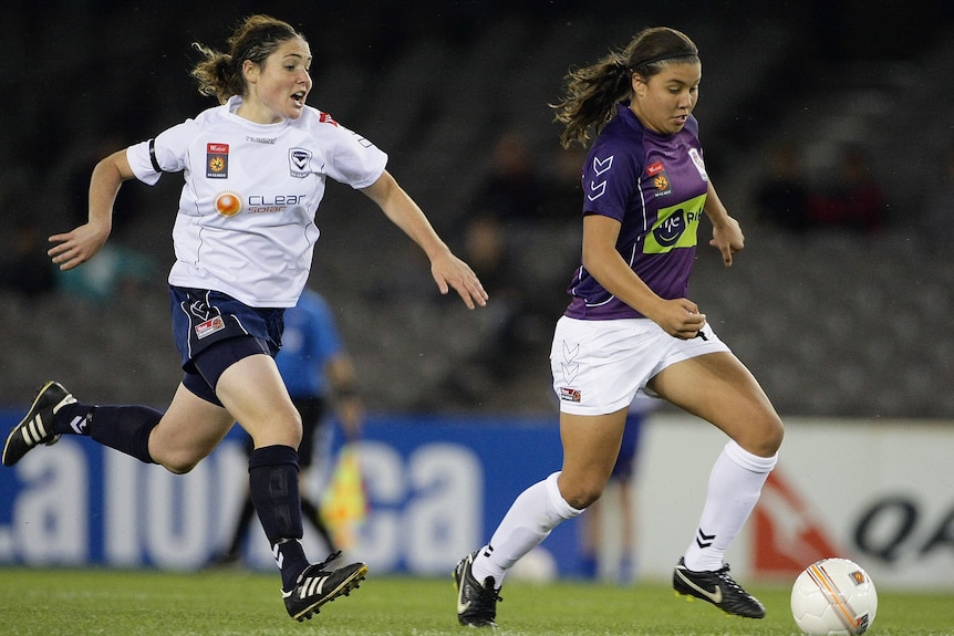 Two female soccer players, one wearing purple and one wearing white, during a game