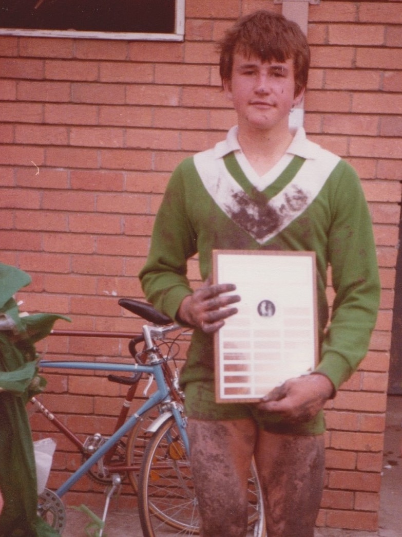 A mud-covered 13-year-old boy holds a plaque with names engraved on it.