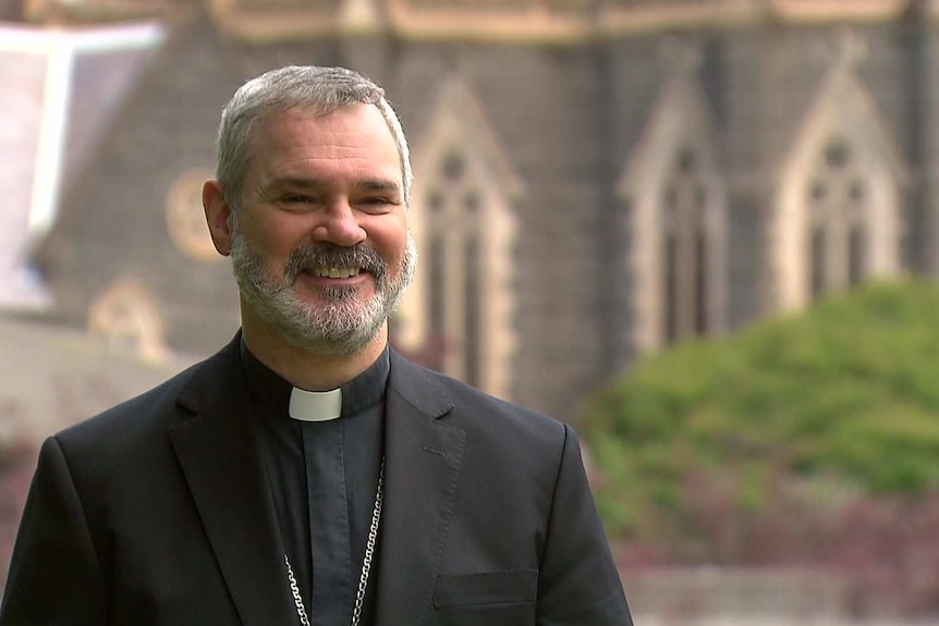 Melbourne Archbishop Peter A Comensoli has a big smile on his face, with St Patrick's cathedral visible in the background.