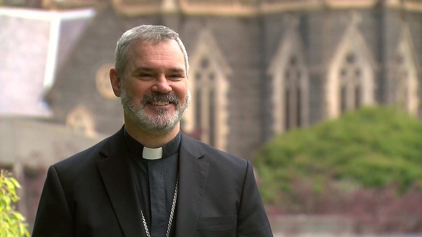 Melbourne Archbishop Peter A Comensoli has a big smile on his face, with St Patrick's cathedral visible in the background.