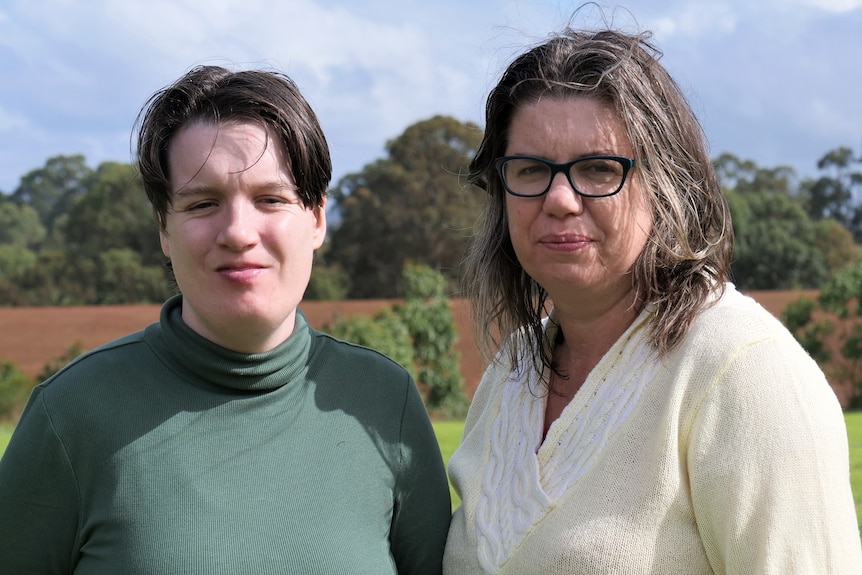 Woman in green turtleneck and short brown hair looks at camera, and her mother is next to her with cream jumper and glasses.