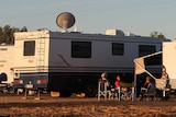 Grey nomads sitting together near their caravans at sundown.