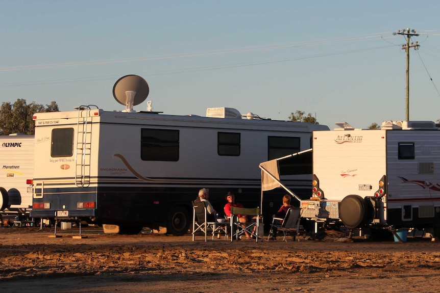 Grey nomads sitting together near their caravans at sundown.