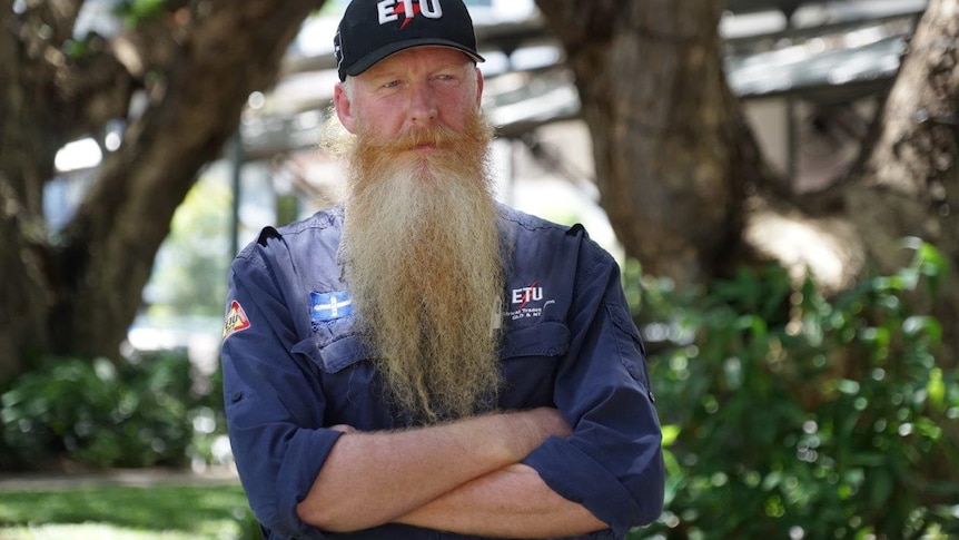 A man with his arms folded and a ETU hat looks seriously at the camera.