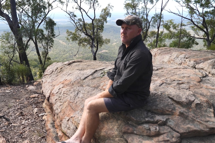 Jason Steele sits on a sandstone outcrop overlooking lightly wooded plains