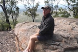 Jason Steele sits on a sandstone outcrop overlooking lightly wooded plains
