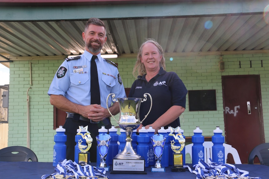 A man and woman stand behind a trophy and water bottles.