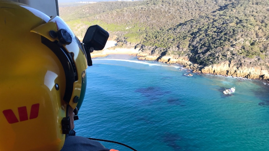 Westpac helicopter rescue personnel overlooking capsized boat
