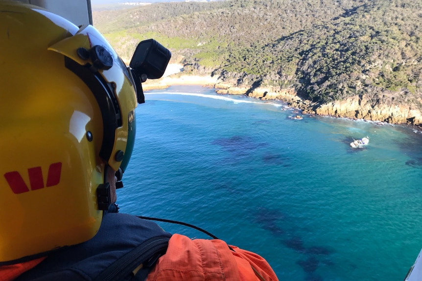 Westpac helicopter rescue personnel overlooking capsized boat
