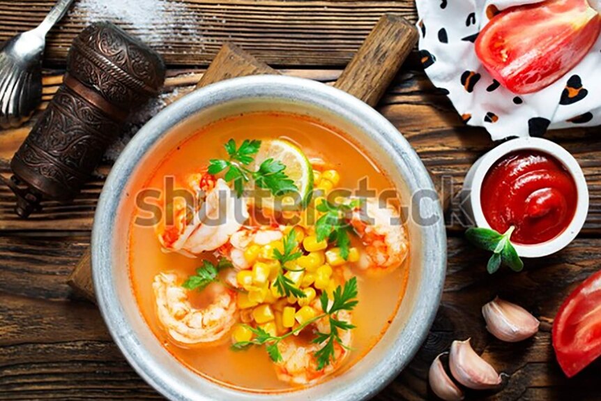 A white bowl full of spicy soup with corn, lime, coriander and prawns.