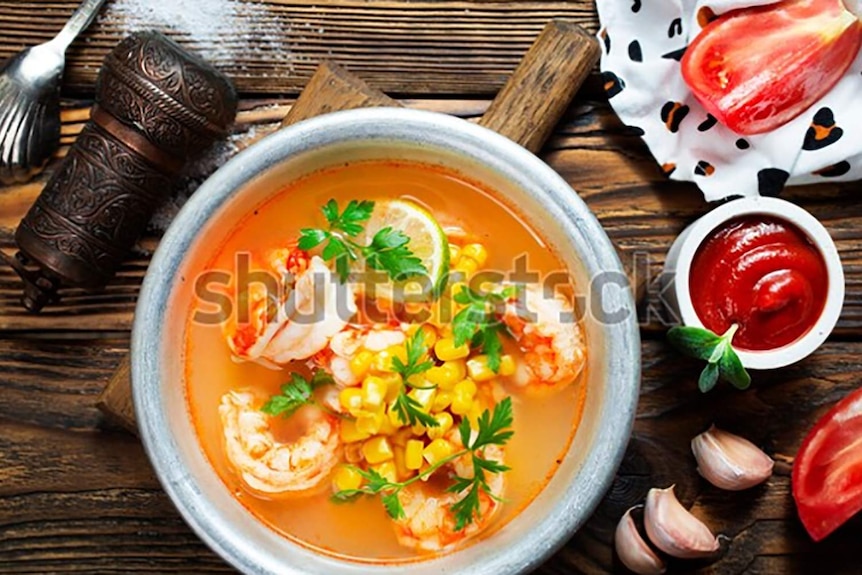 A white bowl full of spicy soup with corn, lime, coriander and prawns.