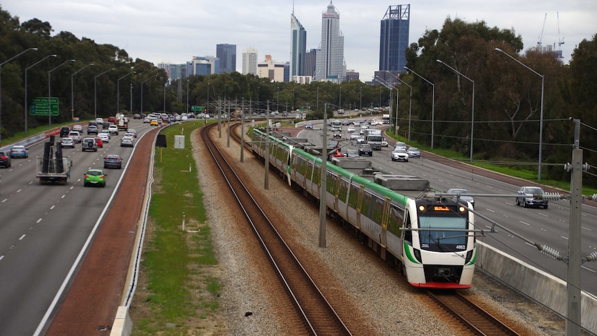 A Transperth train moves south along the freeway with the Perth city skyline in the background