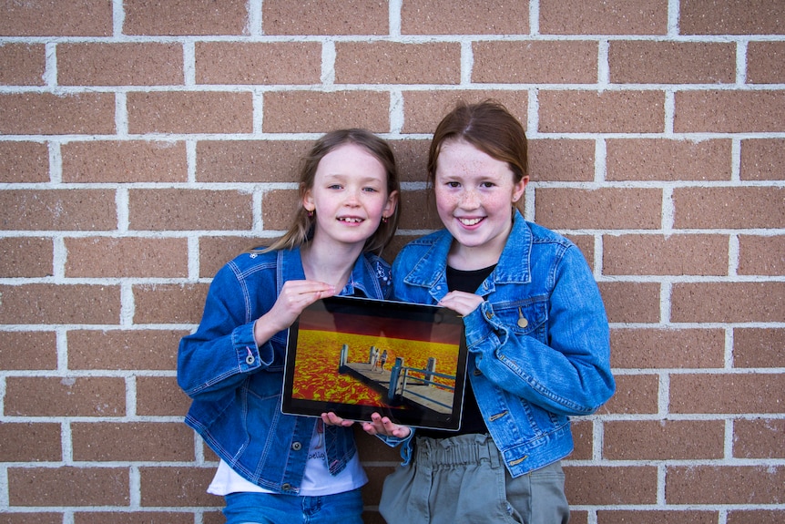 Two young girls hold a picture of a volcano at their Oaks Flat School.