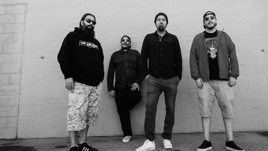 Black and white photo of four members of band Deftones standing side by side against a plain wall