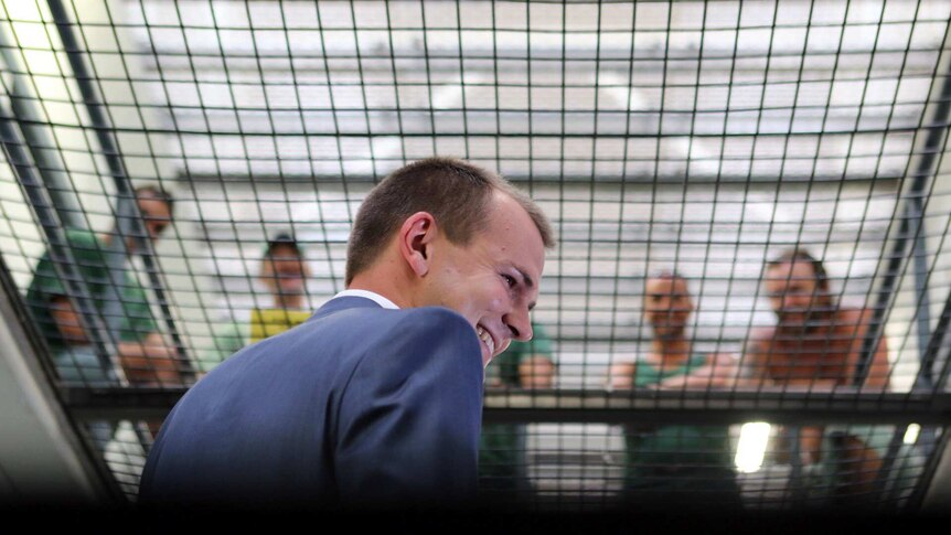 Reporter Jesse Dorsett smiles as prison inmates talk to him from above through metal mesh.