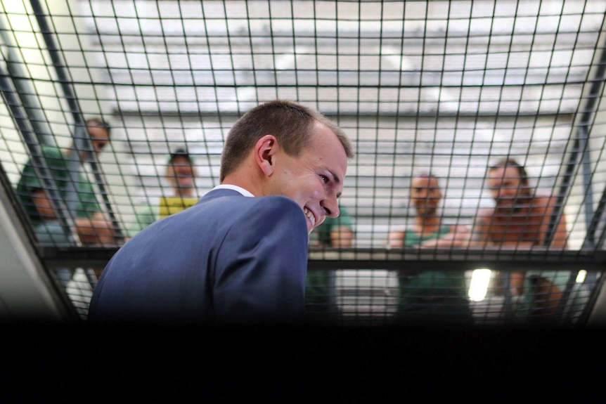 Reporter Jesse Dorsett smiles as prison inmates talk to him from above through metal mesh.