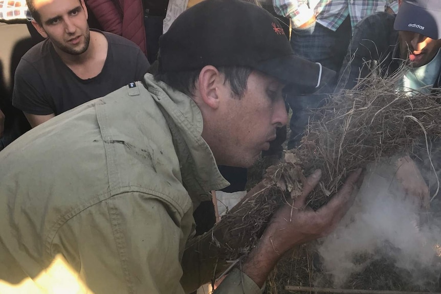 A man blowing on sticks to make fire