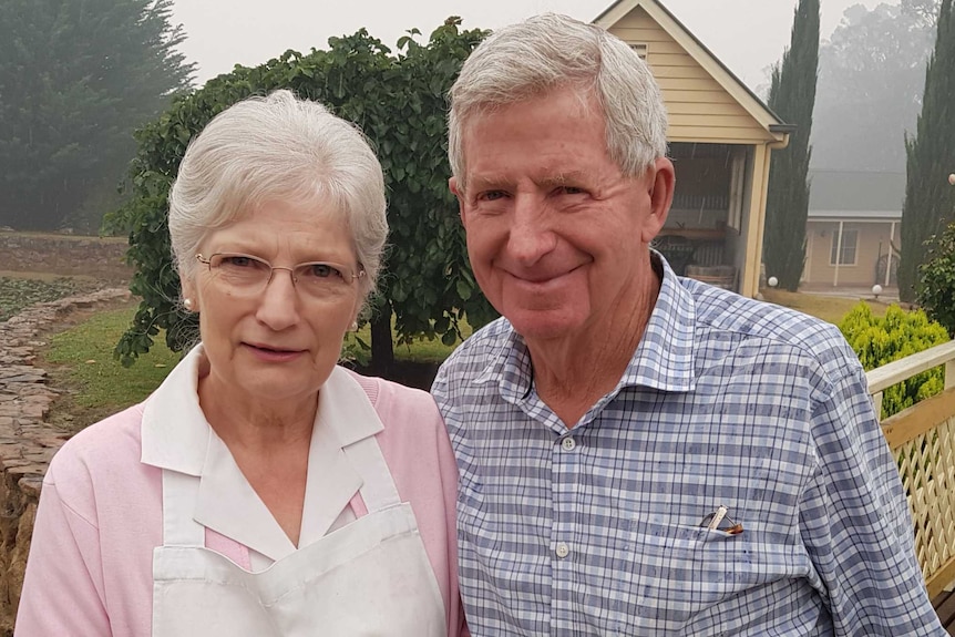 An elderly couple standing on their rural property.