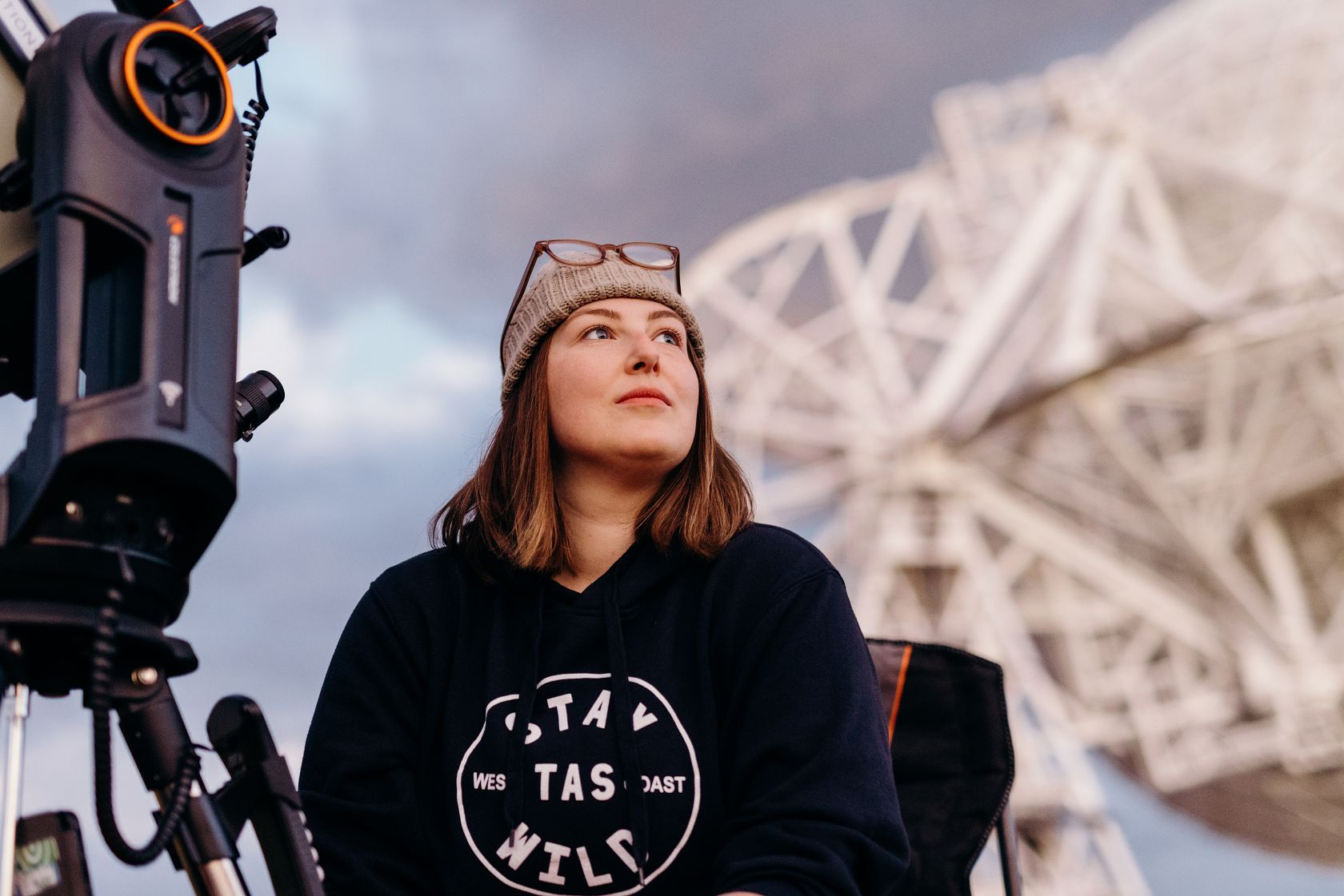 Woman with observation equipment in front of a radio telescope.