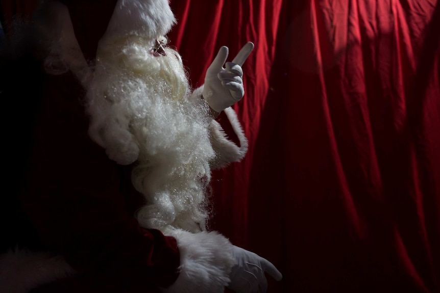 Santa points his finger in profile against a red drape.
