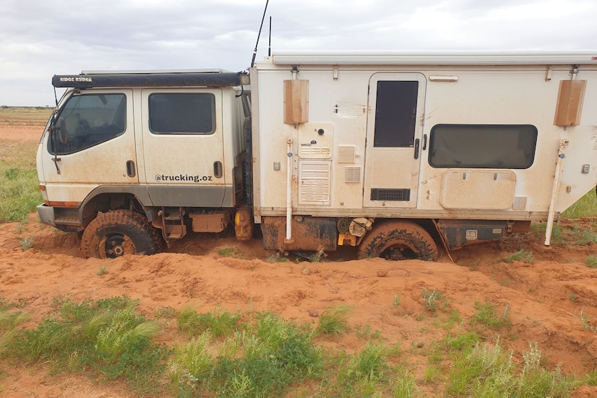 A while campervan covered in mud, in an outback setting. 