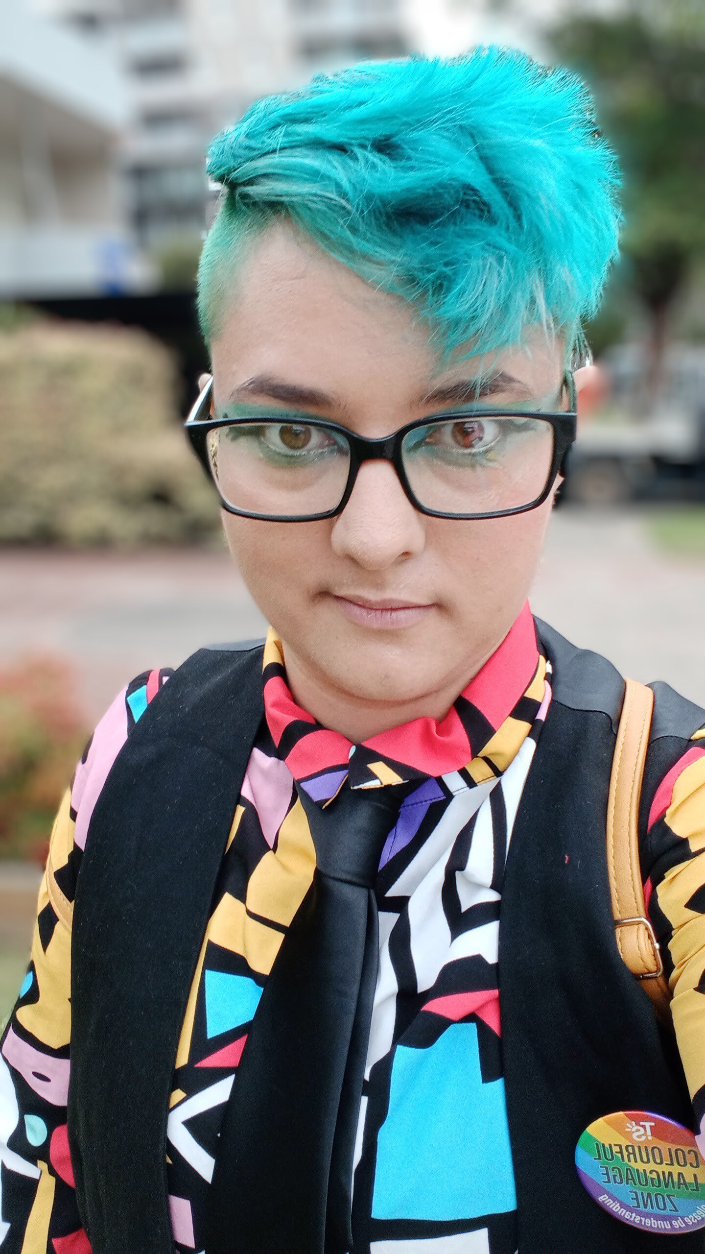 A person with turquoise hair and a colourful shirt smiles gently