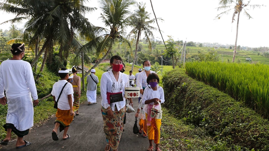 A group of women and girls walking up a narrow street in the Balinese countryside