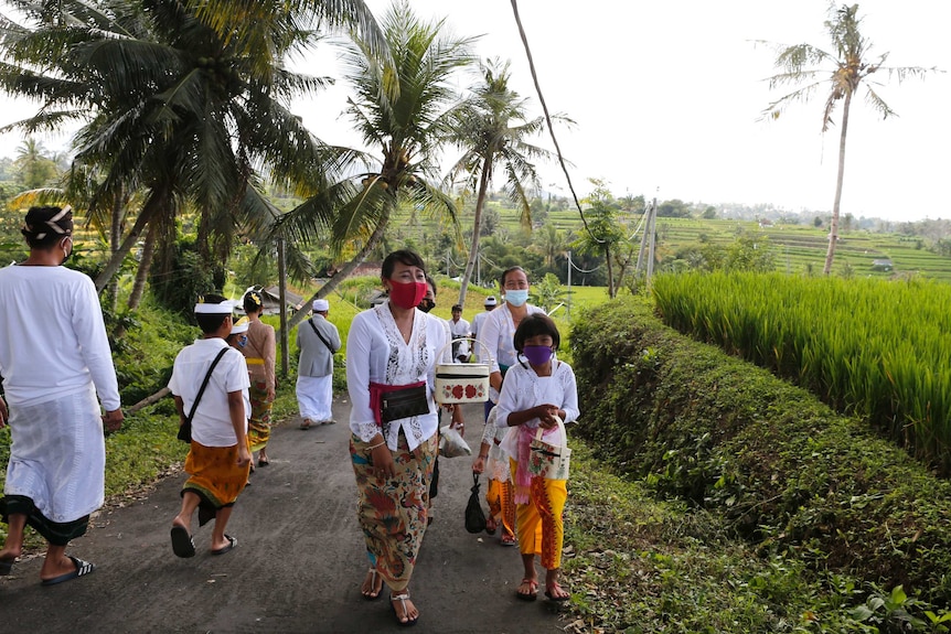 A group of women and girls walking up a narrow street in the Balinese countryside