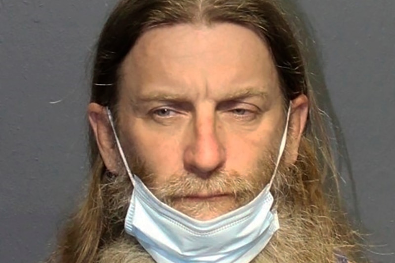 Mug shot of man with long hair and mask pulled down over beard.