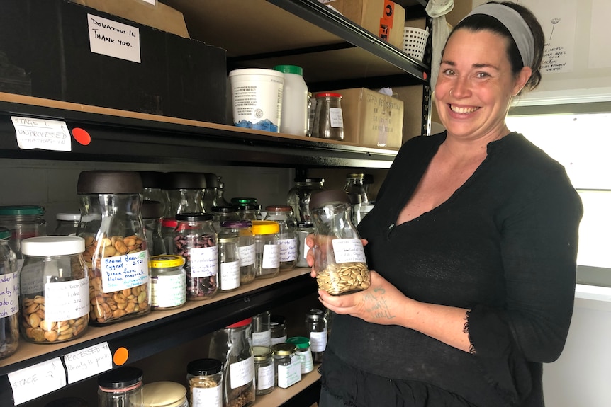 A woman standing in front of a shelf with lots of jars of seeds.