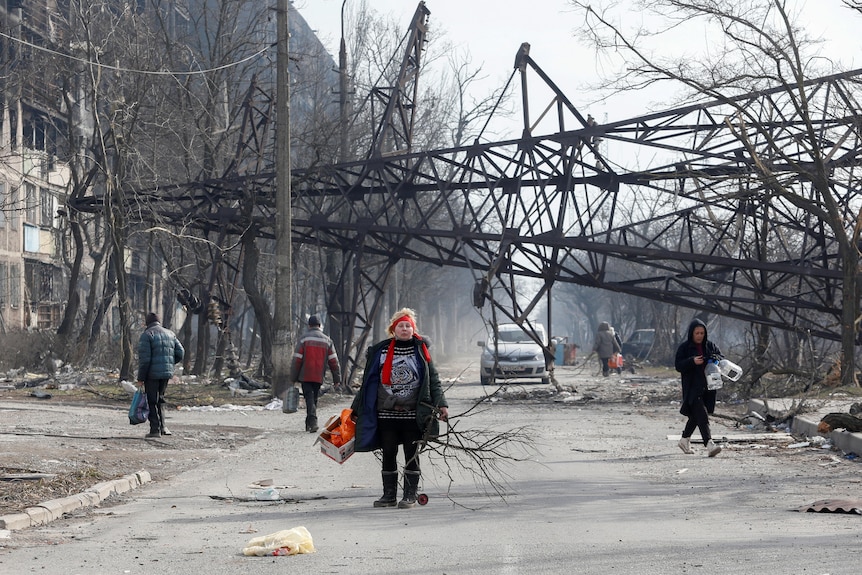 A woman walks on a street with a fallen structure in the background.