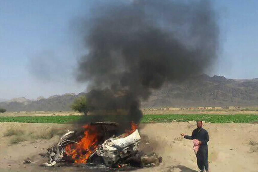 Pakistani people gather around a destroyed vehicle hit by a drone strike.