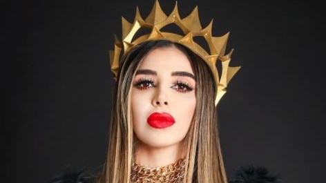 Brunette woman with full, red lips wears black jacket and gold crown