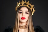 Brunette woman with full, red lips wears black jacket and gold crown