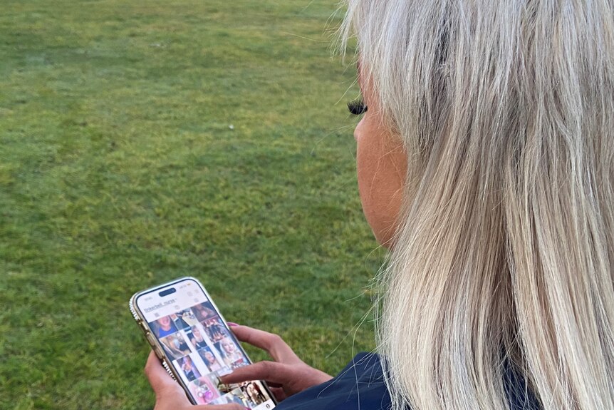 a photo taken over the shoulder of lady with blonde hair, holding mobile phone showing instagram