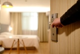 A man's arm opens the door to a hotel room.