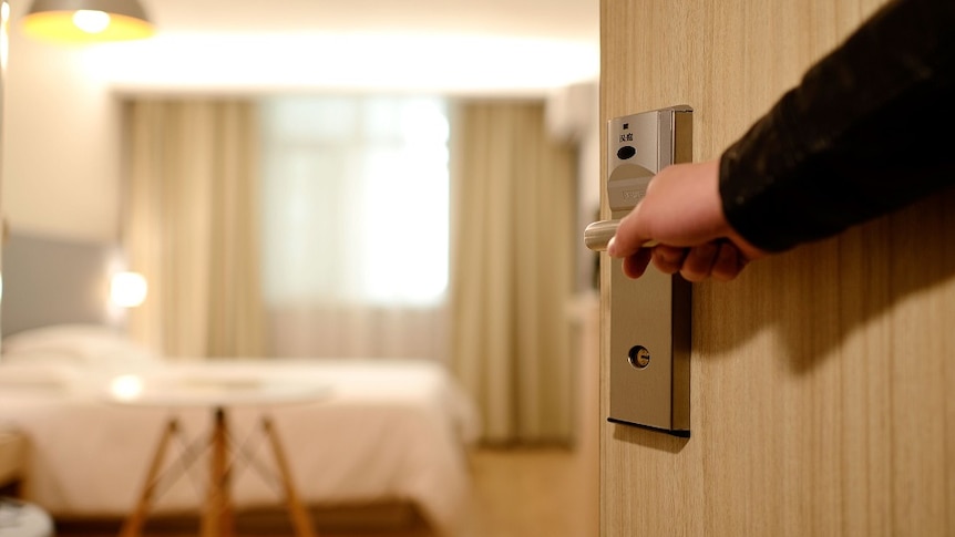 A man's arm opens the door to a hotel room.