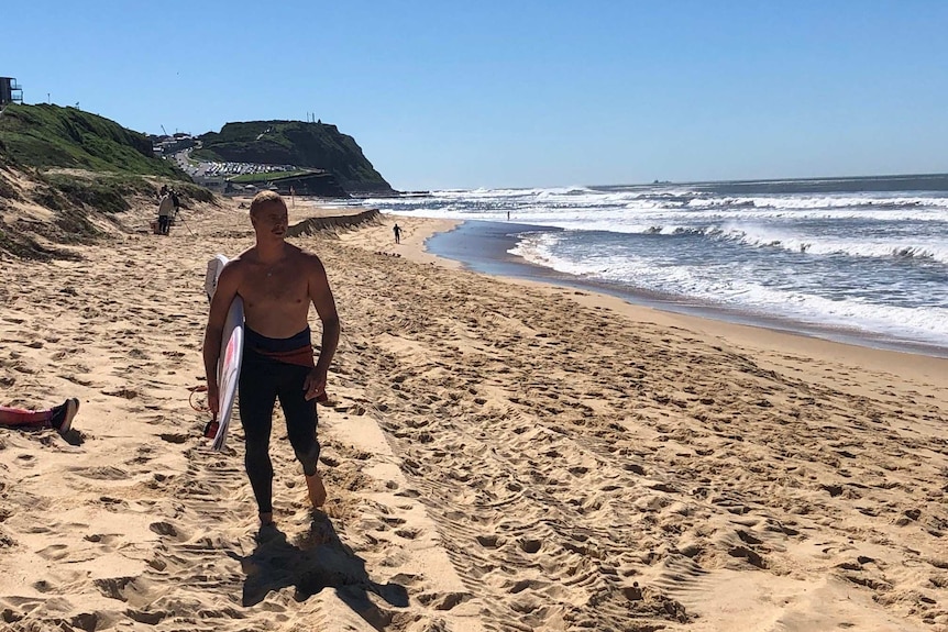 Man walking along beach with surfboard under his arm.