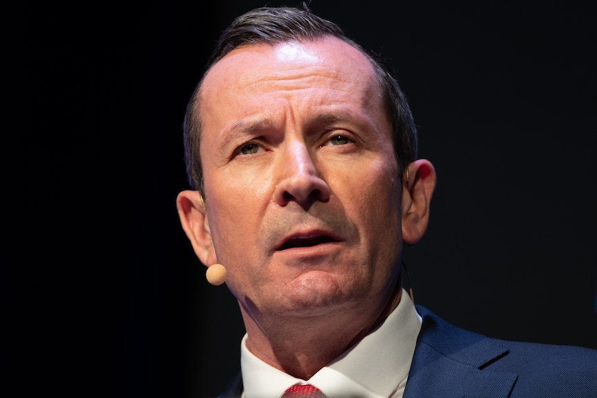 A close-up photo of WA Premier Mark McGowan's face with a microphone next to his right cheek. 