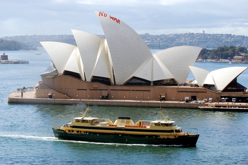 A Sydney ferry moves by the "NO WAR" painted in red on the Sydney Opera House sails
