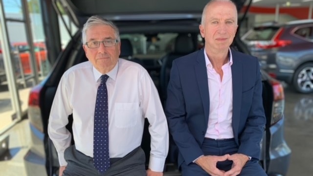 two men in suits sitting next to a car