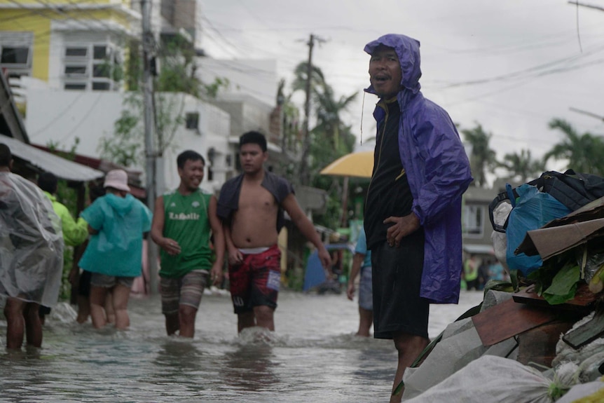 Residents wade along a flooded village wearing plastic rain coats.