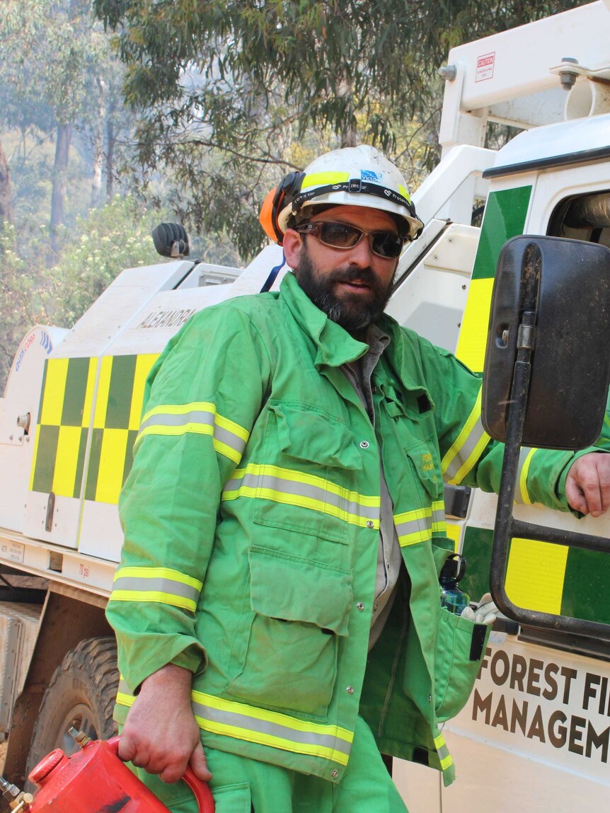 Mat Kavanagh, dressed in green firefighting gear, stands next to a truck in the bush.
