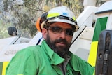 Mat Kavanagh, dressed in green firefighting gear, stands next to a truck in the bush.