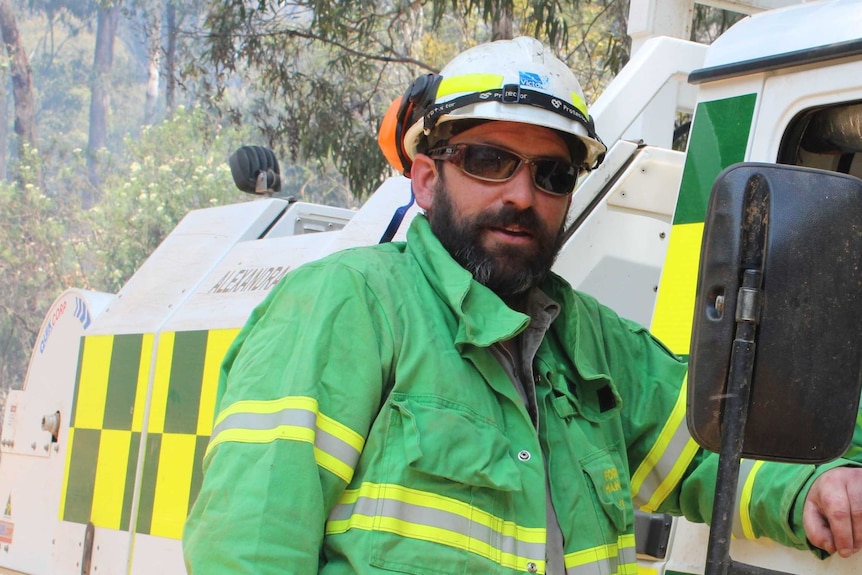 Mat Kavanagh, dressed in green firefighting gear, stands next to a truck in the bush.