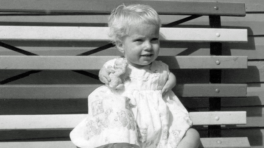 An old photo of a smiling baby in a white frilly dress, with no arms and few fingers.
