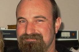 A man with balding brown hair and a beard wearing a black T-shirt